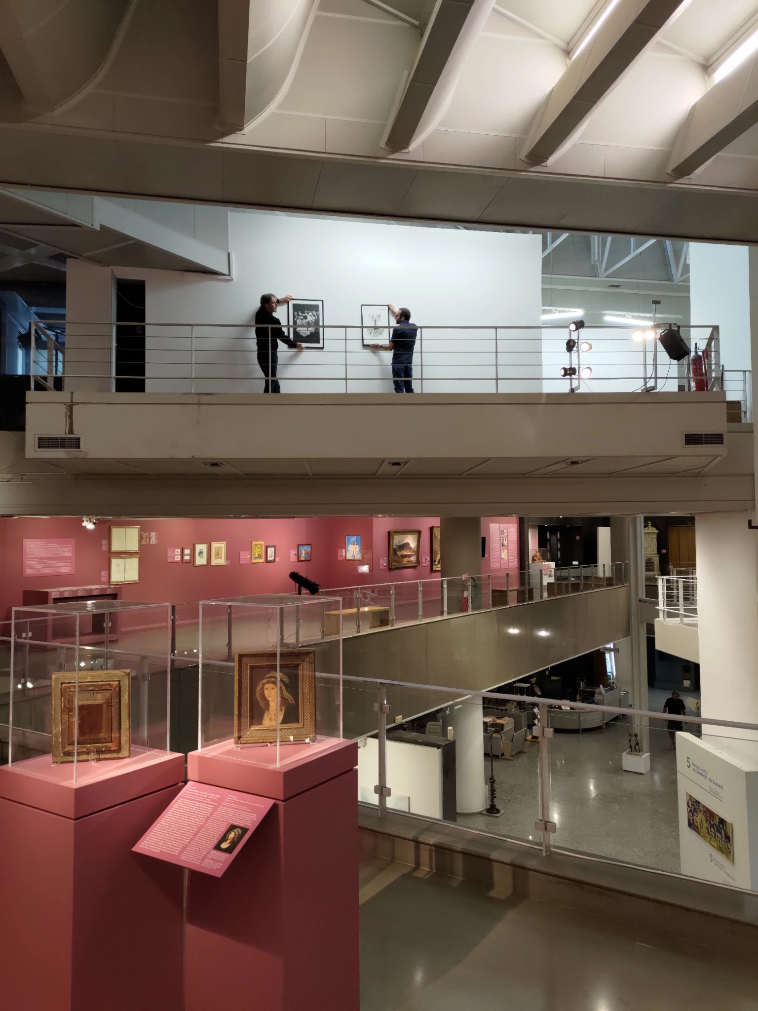 Museum staff hanging Alexandre Mitchell's works on the upper gallery of Teloglion